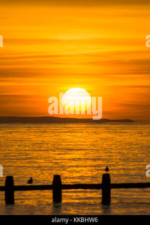 Sonnenuntergang über dem Meer knapp über dem Horizont, auf der britischen Südküste. Stockfoto