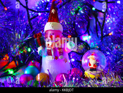 Zauberhafte Weihnachten und Neujahr Karte. Süße Schneemann und Weihnachtsmann in Glaskugel auf farbigen verschwommenen Hintergrund mit Lametta, Girlanden und dekorative Kugel Stockfoto