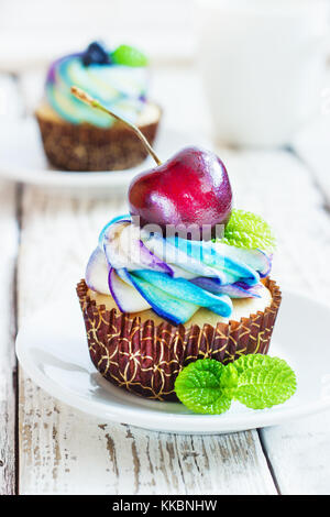 Zarte Vanille Cupcakes mit Sahne und Beeren auf einem weißen Holz- Hintergrund Stockfoto