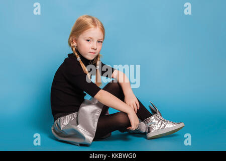 Kleines Mädchen mit Zöpfen in stilvoller Kleidung auf blauem Hintergrund Stockfoto