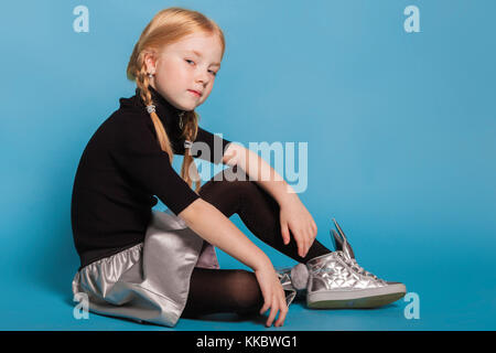 Kleines Mädchen mit Zöpfen in stilvoller Kleidung auf blauem Hintergrund Stockfoto