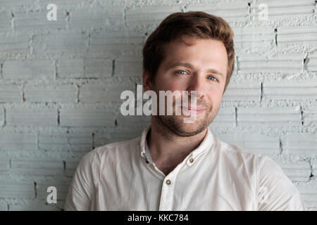 Kaukasische Mann im weißen Hemd in der Nähe von Mauer und lächelt ein wenig. Er Inhalt ist und zuversichtlich. Stockfoto