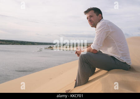 Einsamer Mann sitzen auf Sand Strand und Beobachten weit Blick allein. Stockfoto