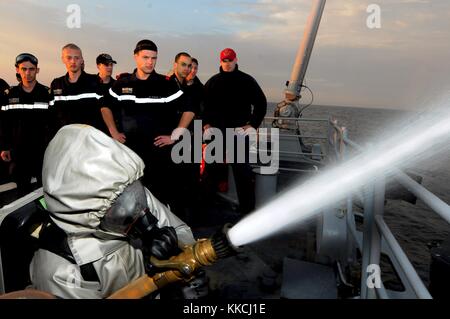 Der Rumpf-Techniker Robert Kinast, rechts, beobachtet einen französischen Seemann, der Feuerwehrtechniken während des Besuchs französischer Seeleute auf dem Lenkraketenkreuzer USS Normandie CG 60, Ostsee, 2012 demonstriert. Foto mit freundlicher Genehmigung der U.S. Navy Foto von Seaman Brian T. Glunt/US Navy. Stockfoto