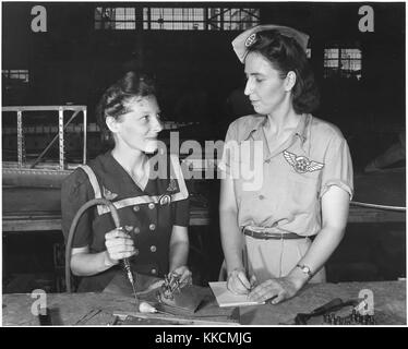 Die Witwen von Pearl Harbor sind in den Krieg gezogen, um den Kampf mit persönlicher Rache fortzusetzen. Frau Virginia Young (rechts), deren Ehemann einer der ersten Opfer des Zweiten Weltkriegs war, ist Vorgesetzter im Assembly and Repair Department der Naval Air Base in Corpus Christi, Texas. Ihre Aufgabe ist es, bequeme und komfortable Wohnräume für Arbeiterinnen aus dem Staat zu finden, wie Ethel Mann, die eine elektrische Bohrmaschine betreibt. Bild mit freundlicher Genehmigung des National Archives. 1942. Stockfoto