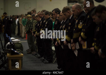 PHILIPPINISCHES MEER (Nov 26, 2017) Matrosen versammeln sich zu einem Gedenkgottesdienst zu Ehren von Aviation Boatswain's Mate (Equipment) Airman Matthew Chialastri, LT. Steven Combs und Aviation Ordnanceman Airman Apprentice Bryan Grosso in der Hangarbucht des vorwärts eingesetzten Flugzeugträgers der Marine, USS Ronald Reagan (CVN 76). Chialastri, Combs und Grosso waren an Bord eines C-2A Greyhound von Fleet Logistics Support Squadron (VRC) 30, als er am 22. November während eines routinemäßigen Transportfluges mit Passagieren und Fracht von der Marine Corps Air Station Iwakuni zur USS Ronald Reagan stürzte. (USA Navy ph Stockfoto