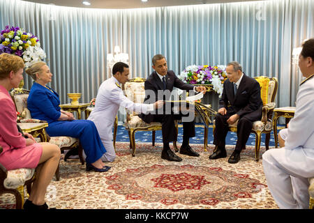 Präsident Barack Obama präsentiert ein Geschenk König Bhumibol Adulyadej von Thailand während ihres Treffens im Siriraj Krankenhaus in Bangkok, Thailand, sep. 18, 2012: Präsident Obama präsentiert ein Fotoalbum mit Fotos des Königs mit der amerikanischen Präsidenten und First Ladies zurückgehen, Präsident Eisenhower. US-Botschafter kristie Kenney mit Außenministerin Hillary Rodham Clinton in Thailand sind auf der linken Seite sitzt. (Offizielle weiße Haus Foto von Pete Souza) diese offiziellen Weißen Haus Foto steht zur Verfügung, die nur für die Veröffentlichung von Nachrichten Organisationen und/oder für den persönlichen Gebrauch drucken mit der s Stockfoto