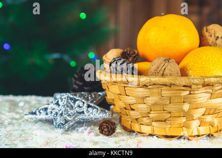 Mandarinen, Nüsse und Stösse in einem Korb auf dem Hintergrund einer Weihnachtsbaum Stockfoto