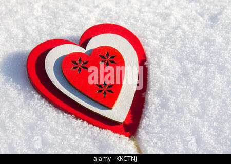 Im Schnee liegt ein rotes Herz aus Holz. Vorlage für eine Weihnachtskarte mit einem weißen Textur und freien Platz für Text Stockfoto