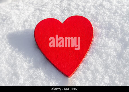 Im Schnee liegt ein rotes Herz aus Holz. Vorlage für eine Weihnachtskarte mit einem weißen Textur und freien Platz für Text Stockfoto