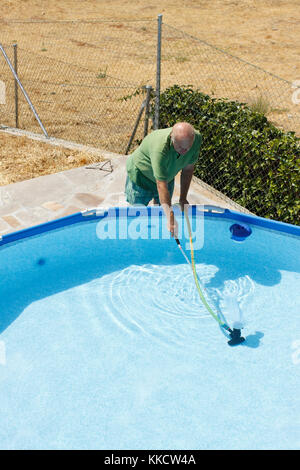 Ein älterer Mann reinigt den Pool im Garten. Stockfoto