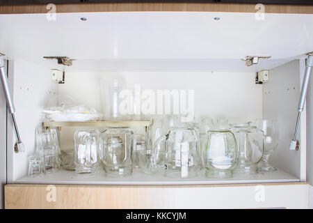 Verschiedene Gläser in einem weißen Schrank auf dem Regal. Banken, Krüge, Gläser, Becher Stockfoto