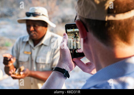 Mann mit Handy Bild der Leitfaden für Sundowner Pirschfahrt im onguma Game Reserve, Namibia, Afrika Stockfoto