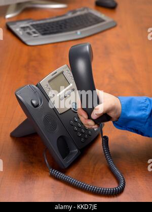 Die menschliche Hand Festnetztelefon an Empfänger in der Hand auf dem Schreibtisch Stockfoto