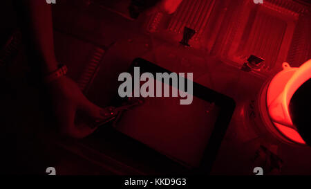 Dunkelkammer-Druck-Prozess Fotograf verwendet Vergrößerer, um fotografische Abzüge zu produzieren. Frau, die in einem roten dunklen Raum arbeitet. Stockfoto