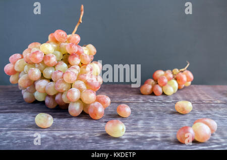 Zwei große und kleine Quasten von Reifen grün-roten Trauben und einige Beeren liegen auf dem dunklen Holztisch. Stockfoto