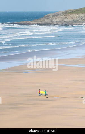 Surfen - Ein Referent aus der Surfschule Surf Schule und eine junge Lerner zu Fuß zum Meer und ein Surfbrett an Fistral Beach Newquay Adr Stockfoto