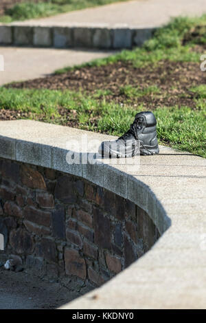 Ein einzelner, schwarzer Lederstiefel, der an einer Steinwand zurückgelassen wurde. Stockfoto