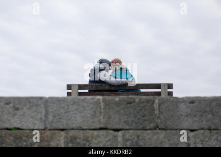Romantisches Paar in der Liebe auf einer Bank sitzen auf Pier umarmen und küssen die Halbinsel Howth, Howth, Dublin, Irland Stockfoto