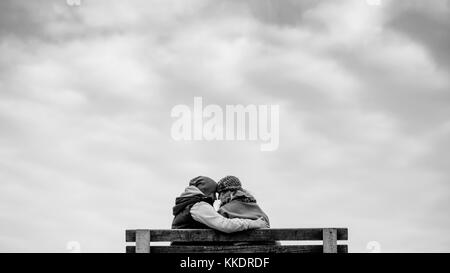 Romantisches Paar in der Liebe auf einer Bank sitzen auf Pier umarmen und küssen die Halbinsel Howth, Howth, Dublin, Irland Stockfoto