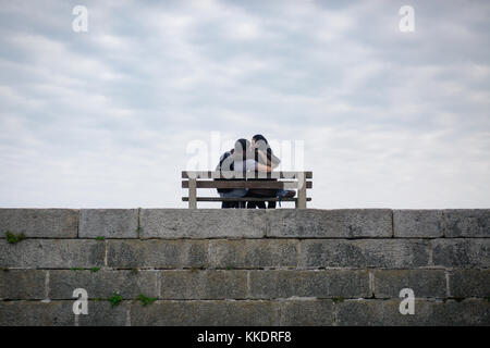 Romantisches Paar in der Liebe auf einer Bank sitzen auf Pier umarmen und küssen die Halbinsel Howth, Howth, Dublin, Irland Stockfoto