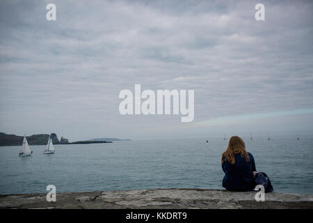 Mädchen allein sitzen auf Pier ist ein Howth Hafen beobachten Yachten entlang der Irischen See, die Halbinsel Howth, Dublin, Irland Stockfoto