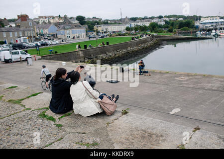 Touristen sitzen auf die howth Hafen Pier Making Memories genießt die Aussicht und die Halbinsel Howth selfies., Dublin, Irland Stockfoto