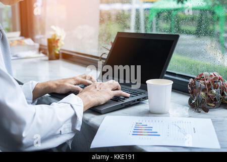 Mockup Bild der Geschäftsmann mit und Tippen auf Laptop mit leerer Bildschirm und Kaffeetasse in der modernen Loft Cafe Stockfoto
