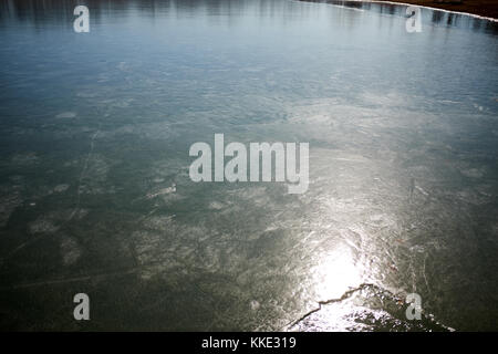 Gefrorene Eis auf einem See oder Fluss von einem Licht beleuchtet die Textur des Ice mit der Reflexion der Vegetation im Hintergrund zu zeigen Stockfoto