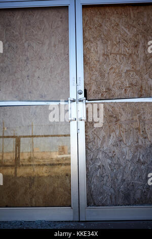 Verbrettert doppelt verglasten Türen in einem verlassenen Gebäude oder Geschäfte in der Nähe zu sehen, mit Reflexionen Stockfoto