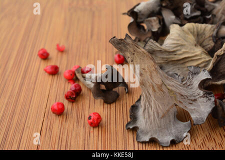 Ein Füllhorn oder craterellus cornucopioides Pilze auf Holz Schneidebrett im Vordergrund mit rotem Pfeffer und getrocknete Pilze im Hintergrund Stockfoto