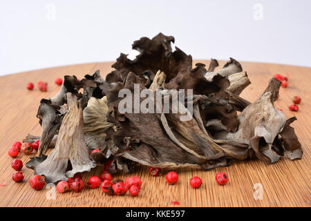 Stapel von getrockneten Füllhorn oder craterellus cornucopioides Pilze mit würzigen roten Pfeffer auf Bambus Holz Schneidebrett auf weißem Hintergrund Stockfoto