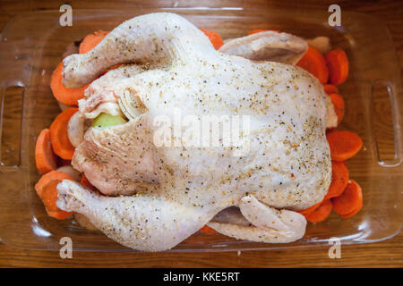 Ein Schuss gewürzte, ungekochte Hühnerstücke, die auf einem Bett aus Karotten in einer Auflaufform angeordnet sind und zum Rösten bereit sind. Mahlzeit-Zubereitungskonzept. Stockfoto
