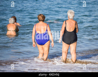 Ältere spanische Frauen, die nach ihrem täglichen Yoga-/Stretching-Kurs am Strand im Meer schwimmen gehen. Stockfoto