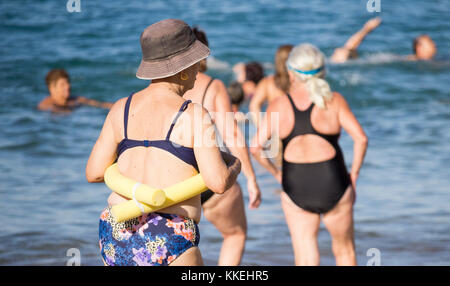 Ältere spanische Frauen, die nach ihrem täglichen Yoga-/Stretching-Kurs am Strand im Meer schwimmen gehen. Stockfoto