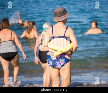 Ältere spanische Frauen, die nach ihrem täglichen Yoga-/Stretching-Kurs am Strand im Meer schwimmen gehen. Stockfoto