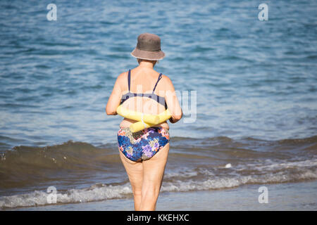 Ältere spanische Frauen, die nach ihrem täglichen Yoga-/Stretching-Kurs am Strand im Meer schwimmen gehen. Stockfoto