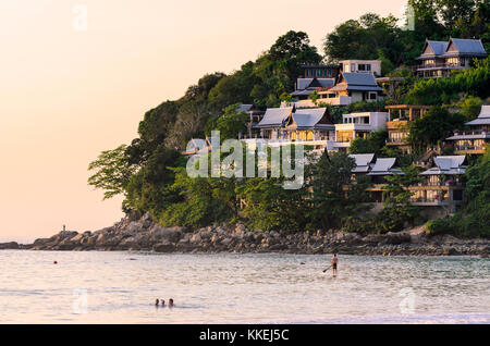 Die felsigen Landzunge am nördlichen Ende von Kamala Beach mit Blick auf die Menschen im Meer bei Sonnenuntergang, Kamala Beach, Phuket, Thailand Stockfoto