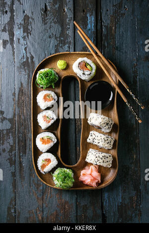 Hausgemachte sushi Brötchen mit Lachs, Sesam und Avocado in Holz Platte serviert mit Rosa eingelegter Ingwer, Sojasauce, Wasabi, Algensalat, Koteletts Stockfoto