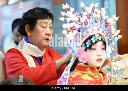 (171205) - LIUZHOU, 5. Dezember 2017 (Xinhua) - Li Fusong, 79, ein pensionierter Lehrer, hilft einem Kind, sich vorzuziehen, um die Peking Oper im Kinderzentrum in Liuzhou, der südchinesischen Autonomen Region Guangxi Zhuang, am 3. Dezember 2017 aufzuführen. Li liebt die Peking-Oper schon seit ihrer Kindheit, bekam aber bis zu ihrer Pensionierung im Jahr 1994 keine Chance, die Oper zu lernen. Während ihres Selbststudiums in den folgenden zehn Jahren stellte sie fest, dass die meisten Opernfans nur ältere Menschen waren. Sie beschloß daraufhin, die traditionelle Kunst mit eigenen Kräften an junge Menschen weiterzugeben. Li geöffnet Stockfoto