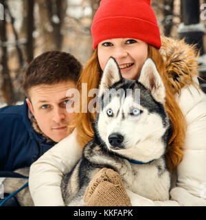 Cute Portrait von fröhlichen schönes Paar umarmen Siberian Husky in den verschneiten Park. Winter. Stockfoto