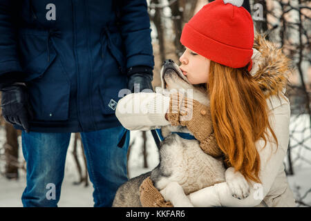 Schönen roten Kopf Frau umarmen und küssen schöne Siberian Husky auf dem Hintergrund der Mann. Winter. Stockfoto