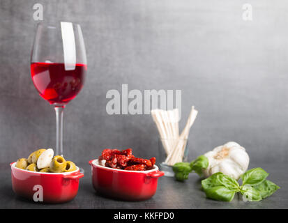 Oliven, getrocknete Tomaten und Rotwein auf grauem Stein Tabelle Stockfoto