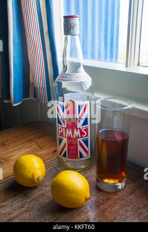 Leere Flasche Pimms mit Glas Pimms trinken und zwei Zitronen auf hölzernen Tisch, Fenster Stockfoto