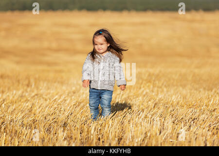 Happy 2 jähriges Mädchen zu Fuß in einer Sommer geernteten Feld Stockfoto