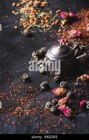 Sortiment von trockenen Tee mit Teesieb als kleine Teekanne. grüner Tee, schwarz Tae, grüner Tee mit Reis, Rooibos, chemische Rosenknospen. Schwarz-strukturiert Schiefer hinterg Stockfoto