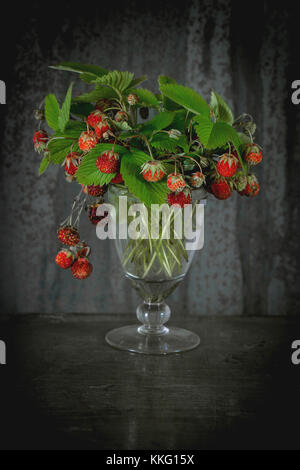 Bündel von Reifen Walderdbeeren mit Blättern in vintage Glas über alte Metall Hintergrund. Landhausstil. Tageslicht. Stockfoto