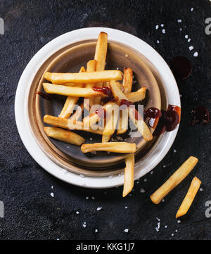 Keramik Teller Pommes Frites mit Salz und Ketchup auf schwarzen Hintergrund, Ansicht von oben Stockfoto