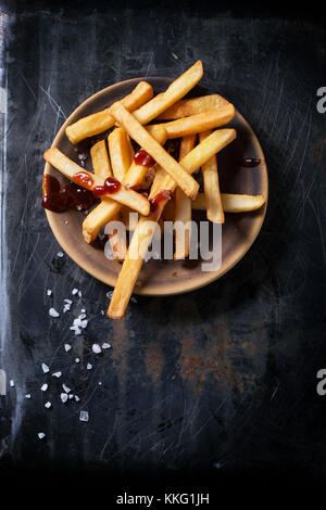 Keramik Teller Pommes Frites mit Salz und Ketchup auf schwarzen Hintergrund, Ansicht von oben Stockfoto