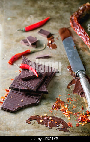 Hacken und Schmelzen dunkle Schokolade mit frischen und trockenen Red Hot Chili Peppers und vintage Messer über alte Metall Hintergrund Stockfoto